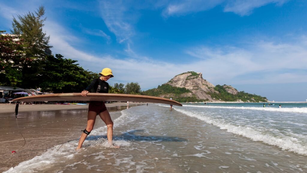 Surfer carrying a longboard along Khao Takiap Beach in Hua Hin