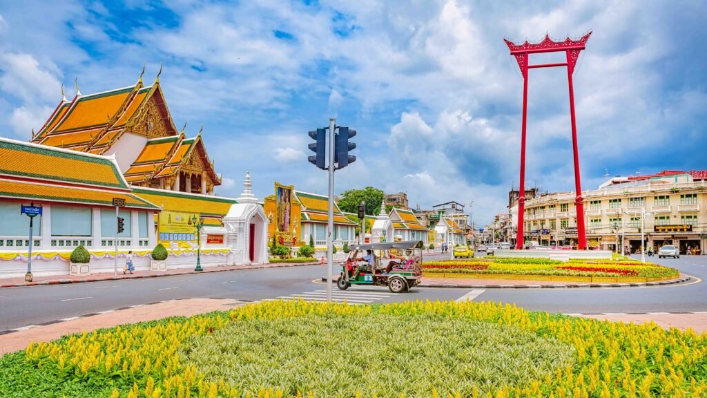 Bangkok’s Giant Swing and Wat Suthat stand beneath a bright blue sky beside a passing tuk-tuk.