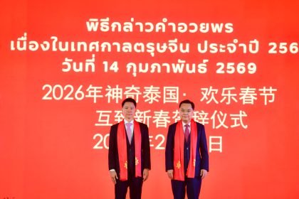 Two senior officials wearing red ceremonial scarves stand on stage before a bright red backdrop displaying Thai and Chinese text for the 2026 Chinese New Year greetings ceremony held on 14 February 2026 in Bangkok.