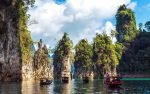 Long-tail boats cruise through limestone cliffs and emerald waters at Khao Sok National Park in Surat Thani, Thailand.